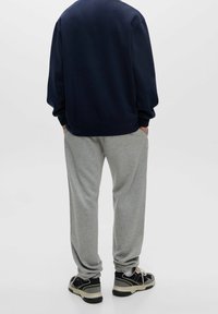 Felpa navy con vestibilità rilassata, abbinata a pantaloni della tuta grigi chiari. Tessuto testurizzato e polsini elastici. Scarpe da ginnastica nere visibili.