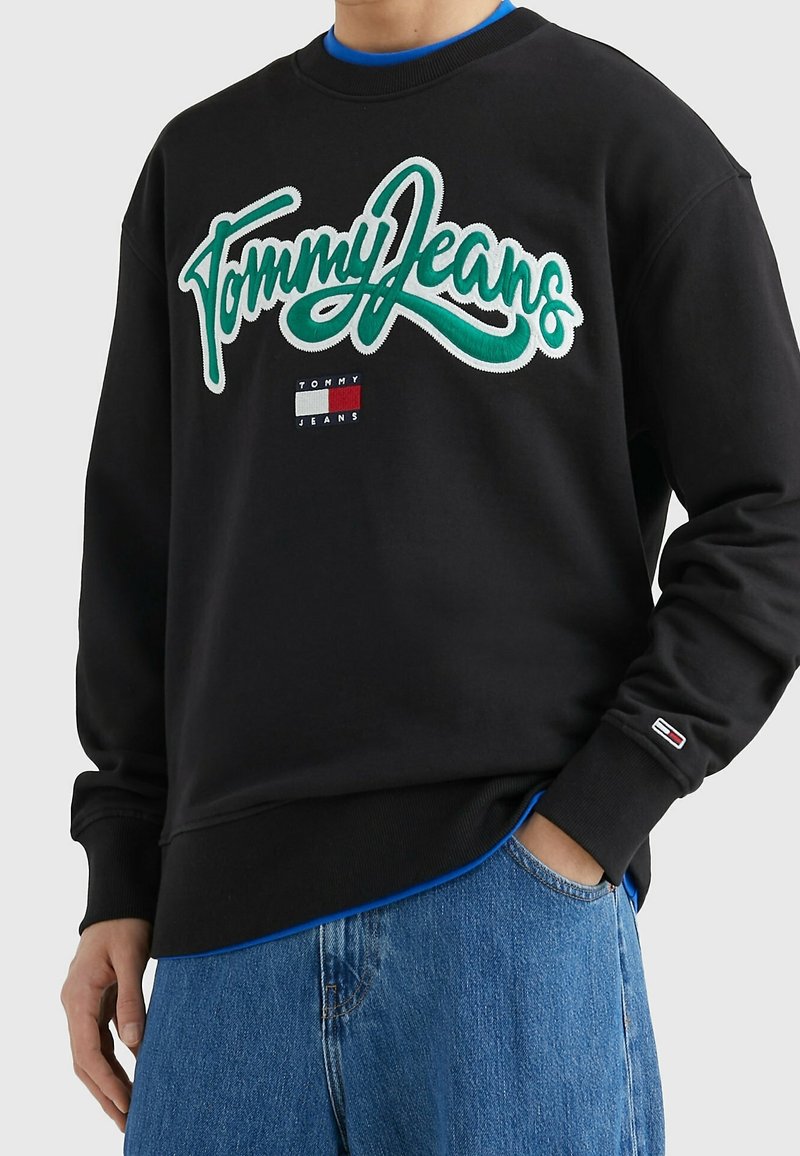 Felpa nera con logo verde "Tommy Jeans". Presenta un accento blu intorno al collo e una piccola etichetta del logo sulla manica sinistra. Materiale in cotone.