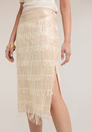 Creme midi nederdel med lagdelt frynse detaljer og en sidelomme, båret med en hvid top og guldarmbånd på venstre håndled.