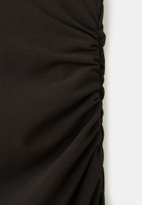 Tissu noir avec un détail froncé rassemblé courant verticalement le long d'un côté sur un fond blanc.