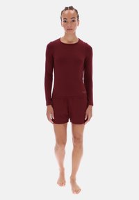 Donkerrode set met een longsleeve top en korte broek, met een gladde textuur en een aansluitend ontwerp. Verfraaid met een subtiel merkembleem op de zoom van de top.