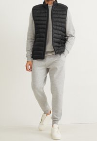 Czarna pikowana kamizelka na jasnoszarej bluzie i pasujących spodniach dresowych. Białe trampki dopełniają strój, tworząc swobodny, warstwowy wygląd.