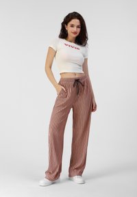Pantalons amples à rayures roses avec une taille à cordon de serrage et des poches latérales, associés à un t-shirt blanc court avec un texte rouge.