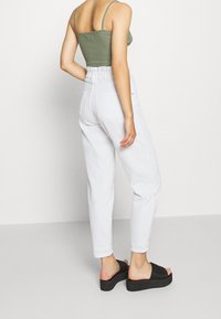 Bílé kalhoty s vysokým pasem a elastickým pasem, spárované se zeleným crop topem. Černé platformové sandály s jemným texturováním.