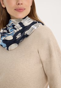 Světle modrý a tmavě námořnický šátek s vzorem z měkké látky, volně přehozený kolem krku. Pod ním je viditelná textura béžového svetru.