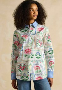 Button-up shirt featuring a floral pattern in red, pink, and blue on a white background, with a light blue striped collar and cuffs.