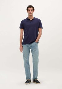 Marineblå polo t-shirt, korte ærmer, blødt stof; lyseblå lige ben jeans; mørke sko med cremefarvede såler. Enkel design, ingen synlige mønstre.