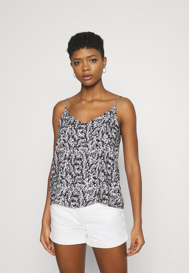 Camisola preta com estampado floral, de alças finas, tecido leve e corte relaxado. Combinada com calções brancos para contraste.