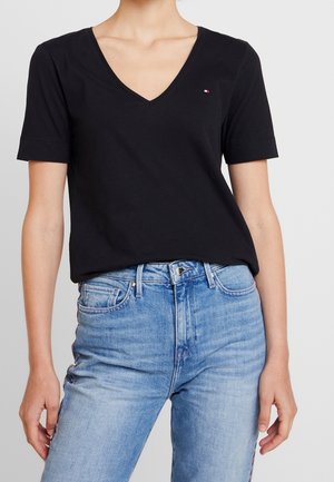 Zwart katoenen T-shirt met een v-hals en korte mouwen, voorzien van een klein logo op de borst. Gecombineerd met lichtblauwe spijkerbroek.