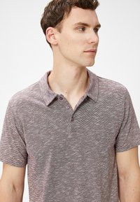 Kurzärmliges Polo-Shirt aus heathered burgundfarbenem Stoff, mit Kragen, drei Knöpfen und subtil gemustertem Textur.