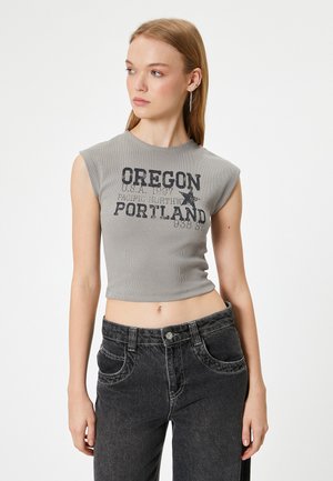 Grå kort tanktop med korte ærmer, prydet med sort grafisk tekst og et stjernedesign. Kombineret med højtaljede sorte jeans.