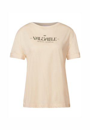 T-shirt crème avec des manches courtes retroussées et un col rond, arborant un texte noir : « VOTRE CHEMIN PRÉCIEUX INFINI / POTENTIEL. »