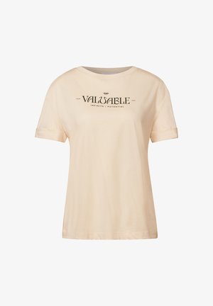 T-shirt crème avec des manches courtes retroussées et un col rond, arborant un texte noir : « VOTRE CHEMIN PRÉCIEUX INFINI / POTENTIEL. »