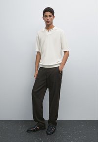 Krátký rukáv, bílý pletený polo, tmavé volné kalhoty a černé sandály na podpatku. Neutrální barvy s jemnými texturovými variacemi.