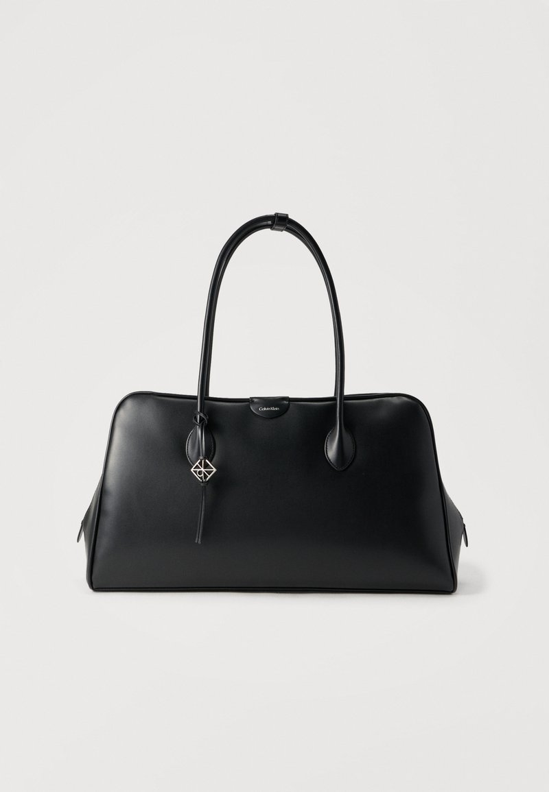 Μαύρη δερμάτινη τσάντα χειρός με δομημένο σχεδιασμό, στρογγυλεμένες λαβές και αποσπώμενο διακοσμητικό με γεωμετρικό μοτίβο. Λεία υφή, ευρύχωρο εσωτερικό.