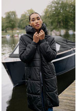 Zwarte gewatteerde jas met een hoge kraag, ritssluiting en elastische manchetten; beschikt over diagonale en horizontale quiltpatronen.