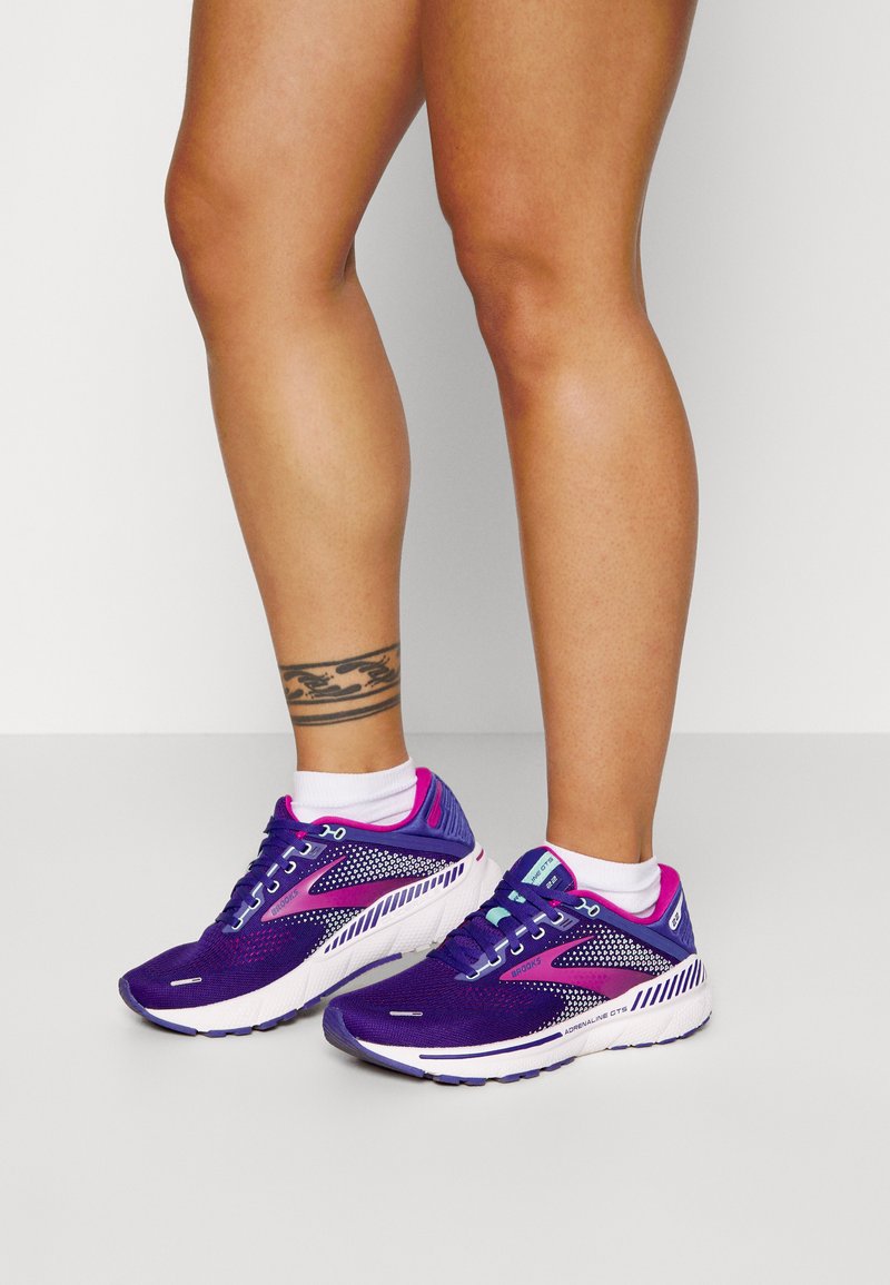 Zapatillas de running moradas con parte superior de malla y acentos en rosa. Cuenta con una suela texturizada y un sistema de cordones para un ajuste seguro.