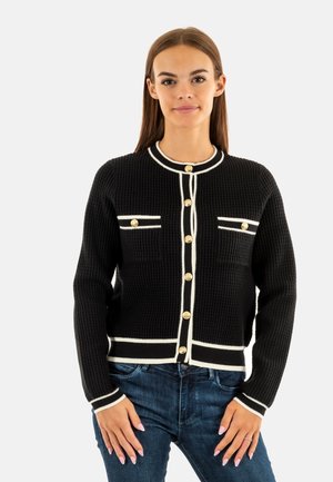 Cardigan de punto negro con ribete blanco, cuello redondo, cierre de botones dorados y dos bolsillos delanteros. Tejido texturizado, estilo ajustado.