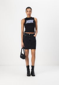 Svart ermeløs topp med hvit "TOMMY JEANS" tekst, kombinert med et svart denim mini-skjørt og svarte ankelstøvler. Liten svart håndveske.