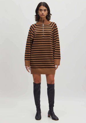 Robe en maille rayée marron et noire avec un col montant et une fermeture éclair. Elle possède des manches longues et une coupe décontractée, associée à des bottes noires jusqu'au genou.