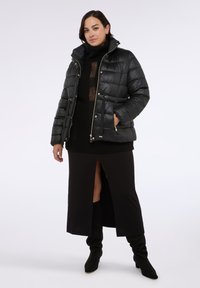 Czarna kurtka puchowa o błyszczącym wykończeniu, z zamkiem błyskawicznym i sznureczkami, zestawiona z czarnym swetrem z dzianiny oraz regulowanymi kozakami za kolano.