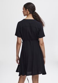 Robe noire à manches courtes, décontractée, avec une taille cintrée et une jupe fluide qui arrive à mi-cuisse. Texture de tissu lisse.