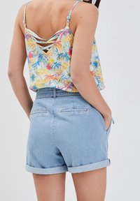 Débardeur à motifs floraux avec des motifs de palmiers multicolores et un détail croisé dans le dos, associé à un short en denim bleu clair avec des revers retroussés.