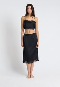 Czarny satynowy komplet składający się z topu na krótki rękaw z koronkowym wykończeniem oraz spódnicy do kostek z koronkowym brzegiem. Gładka tekstura, regulowane ramiączka.