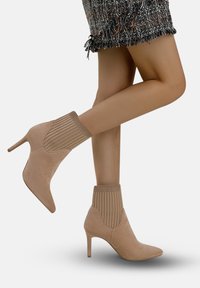 Stivaletti in suede beige con punta affusolata e parte superiore in maglia a coste. Presentano un tacco a stiletto e una texture liscia.
