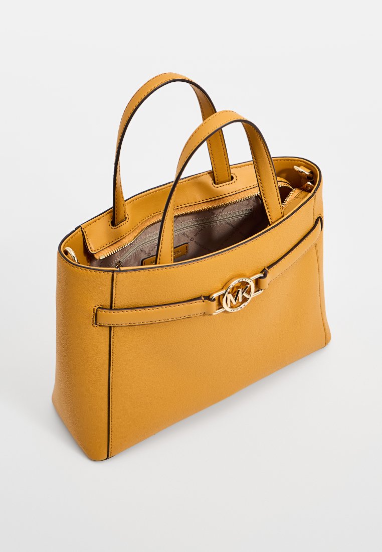 Sac à main en cuir jaune moutarde avec double anses, logo doré MK et poche zippée intérieure, présenté en angle latéral sur fond blanc.