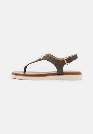 Bruine Michael Kors teenslipper met logopatroon, gouden gesp en logohanger op een witte rubberen zool.