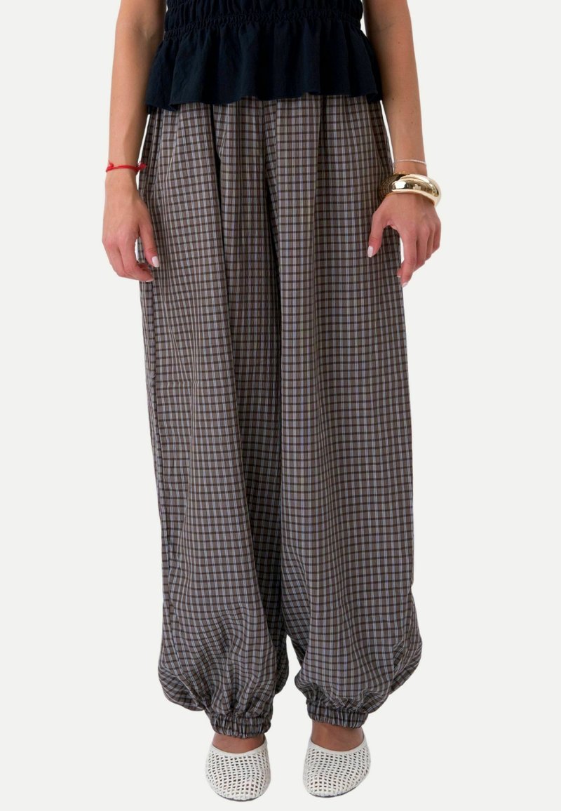 Femme portant un pantalon large à carreaux avec des poignets élastiques, un top noir, des chaussures blanches sans lacets et des bracelets aux deux poignets.