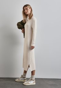 Vestito a maglia beige a coste con maniche lunghe e spacchi laterali. Abbinato a sneakers beige e bianche e calzini di colore chiaro.