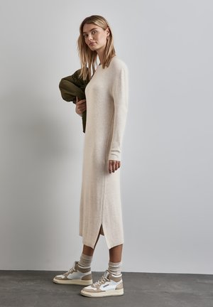 Robe pull beige à côtes avec des manches longues et des fentes sur les côtés. Associée à des baskets beige et blanches et des chaussettes de couleur claire.