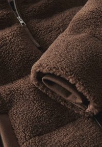 Braune Fleecejacke mit einer weichen, strukturierten Außenseite und einem glatten Innenfutter, mit einem Reißverschluss und subtilen tonalen Akzenten.