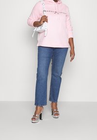 Vaaleanpunainen huppari, jossa musta logo, siniset suorat farkut ja metallinhohtoiset hopeiset korkokengät paksulla korolla. Valkoinen käsilaukku.