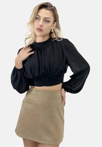 Schwarzes Crop-Top mit langen Ärmeln, Plisseedesign und geraffter Taille, kombiniert mit einem hellbraunen Minirock aus Wildleder mit dezenten Steppnähten.