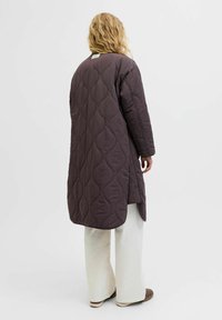 Abrigo largo acolchado en púrpura oscuro, con un patrón texturizado, hombros caídos y aberturas laterales, combinado con pantalones acampanados en blanco roto.