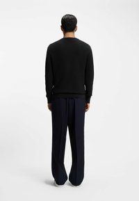 Czarny sweter o fakturze z okrągłym dekoltem, ściągaczami na rękawach i dole, w połączeniu z granatowymi spodniami o szerokich nogawkach i białymi trampkami. Widok z tyłu.