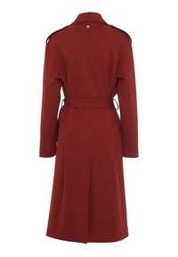 Long manteau rouge en tissu texturé, doté d'une ceinture, d'épaulettes et d'une fente centrale à l'arrière. Design épuré et affûté.