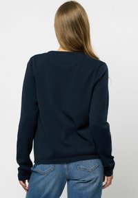 Hanorac bleu marin cu mâneci lungi, guler rotund, material texturat și manșete ribbate. Purtați cu pantaloni din denim bleu deschis.