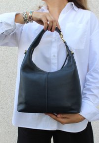 Svart läder hobo-väska med en slät yta, rund topphandtag, detaljer i guld och dragkedjestängning längs toppen.