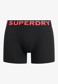 Boxers en coton noir avec une large ceinture élastique portant l'inscription "SUPERDRY" en lettres rouges vives. Texture lisse, coupe ajustée.