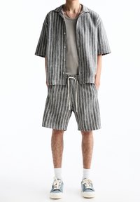 Chemise à manches courtes rayée en gris et blanc, associée à un short assorti. Tissu en coton, coupe décontractée, avec taille à cordon et baskets.