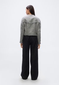 Σύντομο γκρι σακάκι από καρό υφαντό ύφασμα με ξεφτισμένα άκρα και διακριτικό ραχιαίο γιακά. Συνδυάζεται με μαύρο παντελόνι φαρδιάς γραμμής. Υφή υφάσματος με διακριτικό μοτίβο.