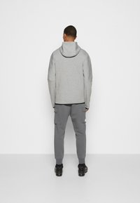 Grå hoodie med huva, sittande ärmar och grå cargobyxor. Båda plaggen har en slät yta och en enkel design utan mönster.