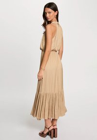 Beige maxi dress with a pleated skirt, sleeveless design, and tied detail at the back. Finished with textured fabric and a flowy silhouette.