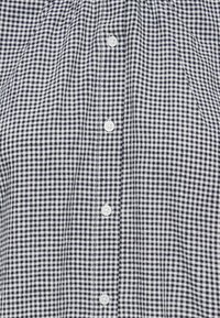 Devant de chemise à petit motif à carreaux noir et blanc avec des boutons blancs espacés régulièrement au centre.