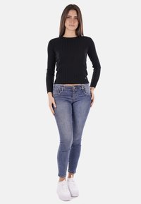 Maglietta a maniche lunghe crop nera a coste abbinata a jeans skinny blu e sneakers bianche. Dettagli notevoli includono il design aderente e il tessuto testurizzato.