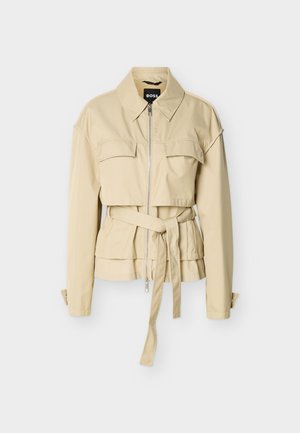 Μπεζ μπουφάν με φερμουάρ, δύο τσέπες στο στήθος με καπάκι, ζώνη στη μέση, μακριά μανίκια με μανσέτες με κουμπιά και αιχμηρό γιακά.